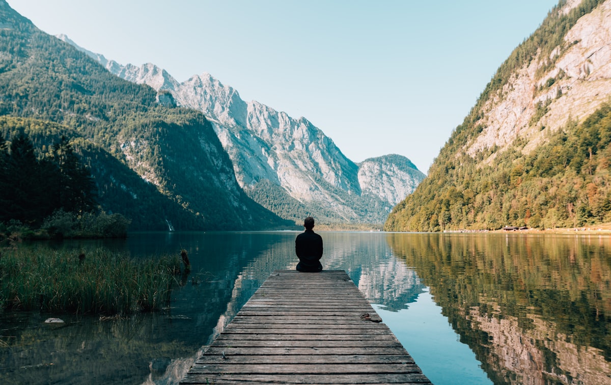 Člověk sedící na molu s výhledem na jezero a hory